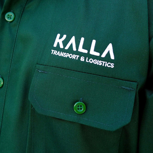 Close-up of a green work uniform shirt with KALLA Transport & Logistics logo embroidery.